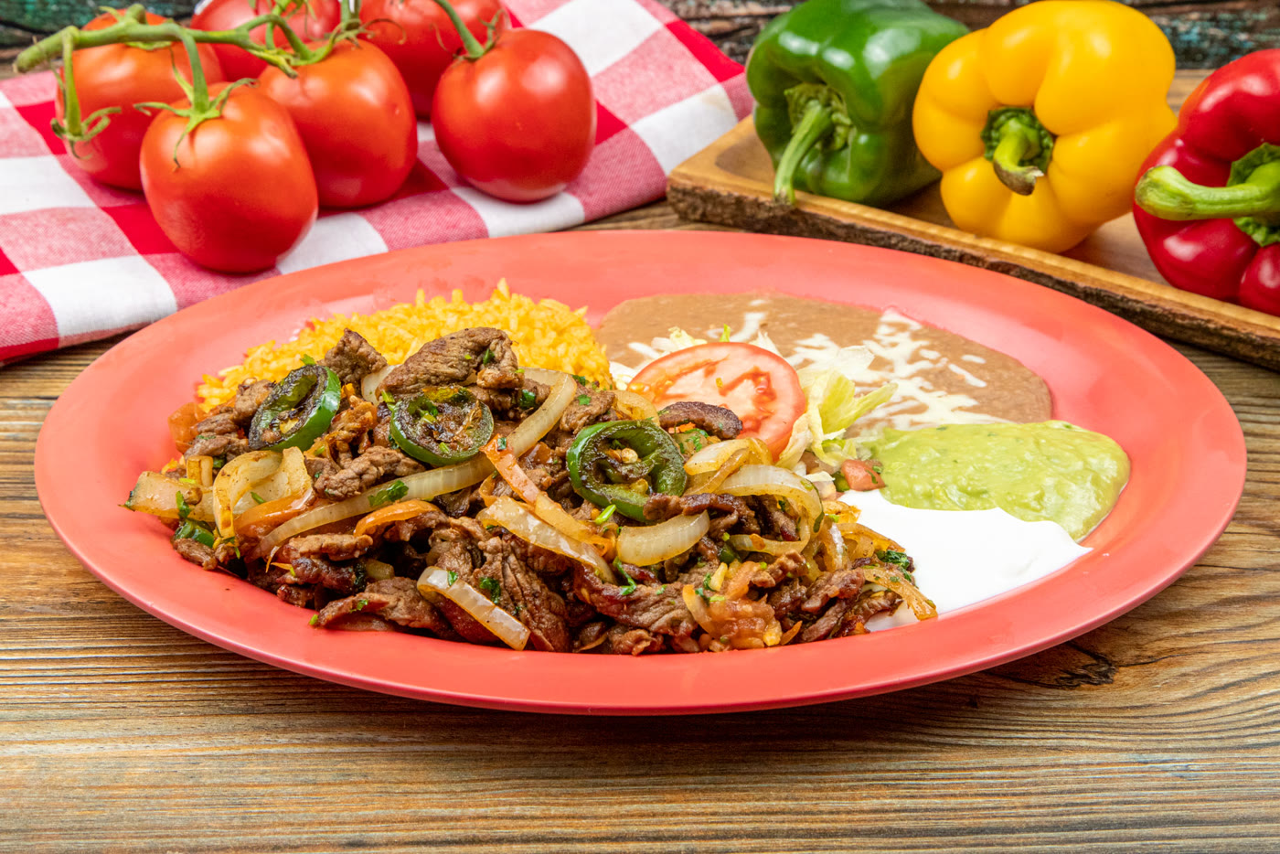 A carne asada plate of sliced beef steak with grilled jalape&ntilde;os and onions, served with rice, beans, guacamole, sour cream and tomato.